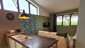A modern kitchen with a central island, a dining area with a sofa, and a large window offering a view of the outdoors. - Cozy cottage in Athienville (Athienville)