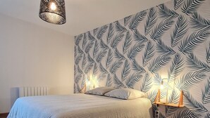 A bedroom with a bed, a patterned wall, a radiator, and a hanging light fixture. - Cozy cottage in Athienville (Athienville)
