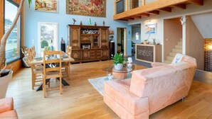 Un vaste espace de vie doté d’un haut plafond, une table à manger avec des chaises, un canapé rose et un grand tableau accroché au mur.