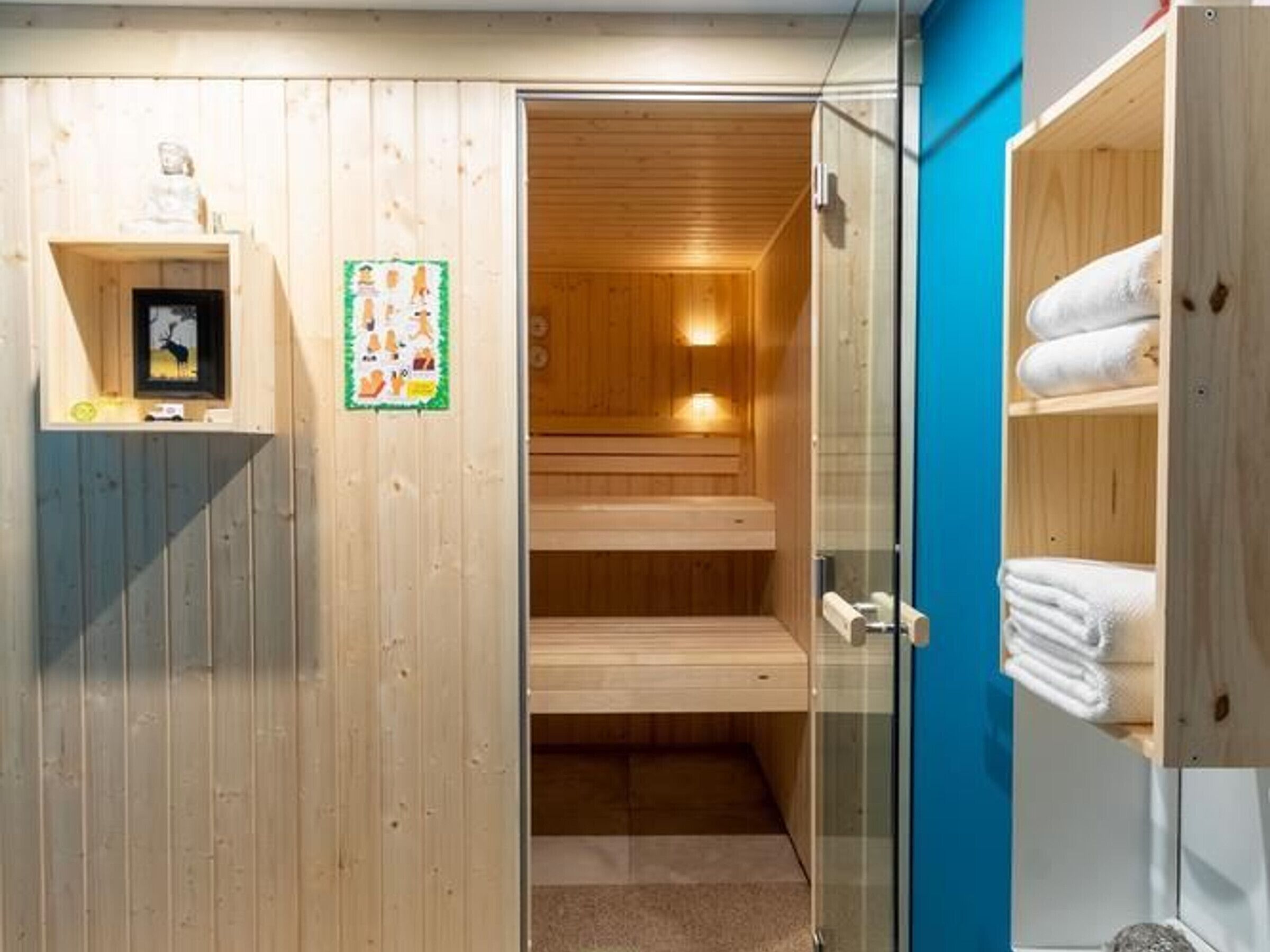 Un sauna avec des murs et des bancs en bois, une porte en verre et une étagère où sont rangées les serviettes.