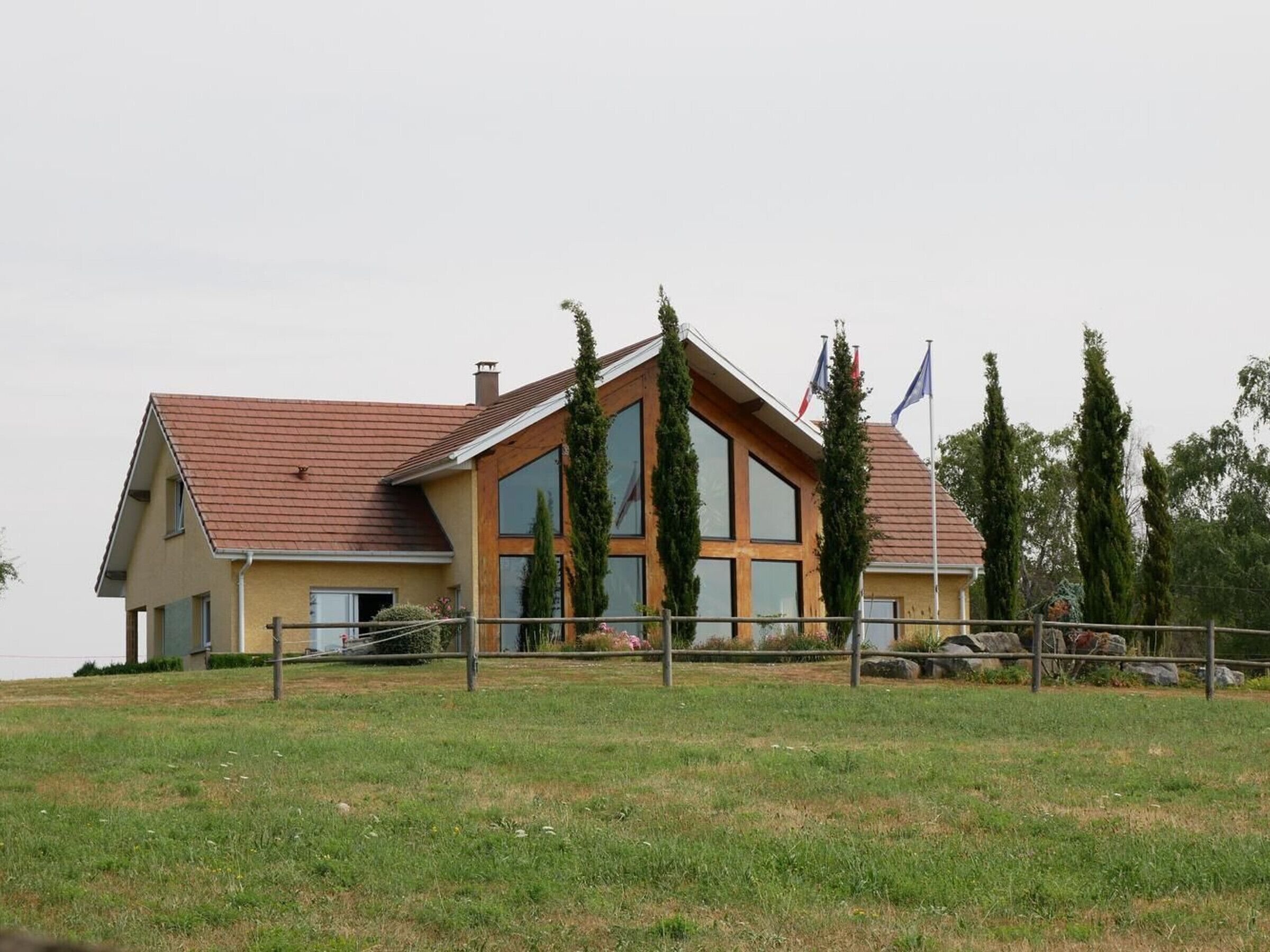 Ein zweistöckiges Gebäude mit schrägem Dach, großen Fenstern und einem eingezäunten Vorgarten.