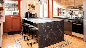 Une cuisine moderne dotée d’un îlot en marbre, de tabourets de bar, d’une cuisinière à gaz et d’un dosseret carrelé.