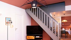 Un salon moderne avec un escalier, un téléviseur à écran plat et un coin repas avec une table mise pour deux personnes.