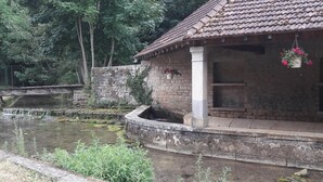 A rustic building with a tiled roof, a stone wall, and a small water feature. - Cozy room in historic house with park and horse facility (Choye)