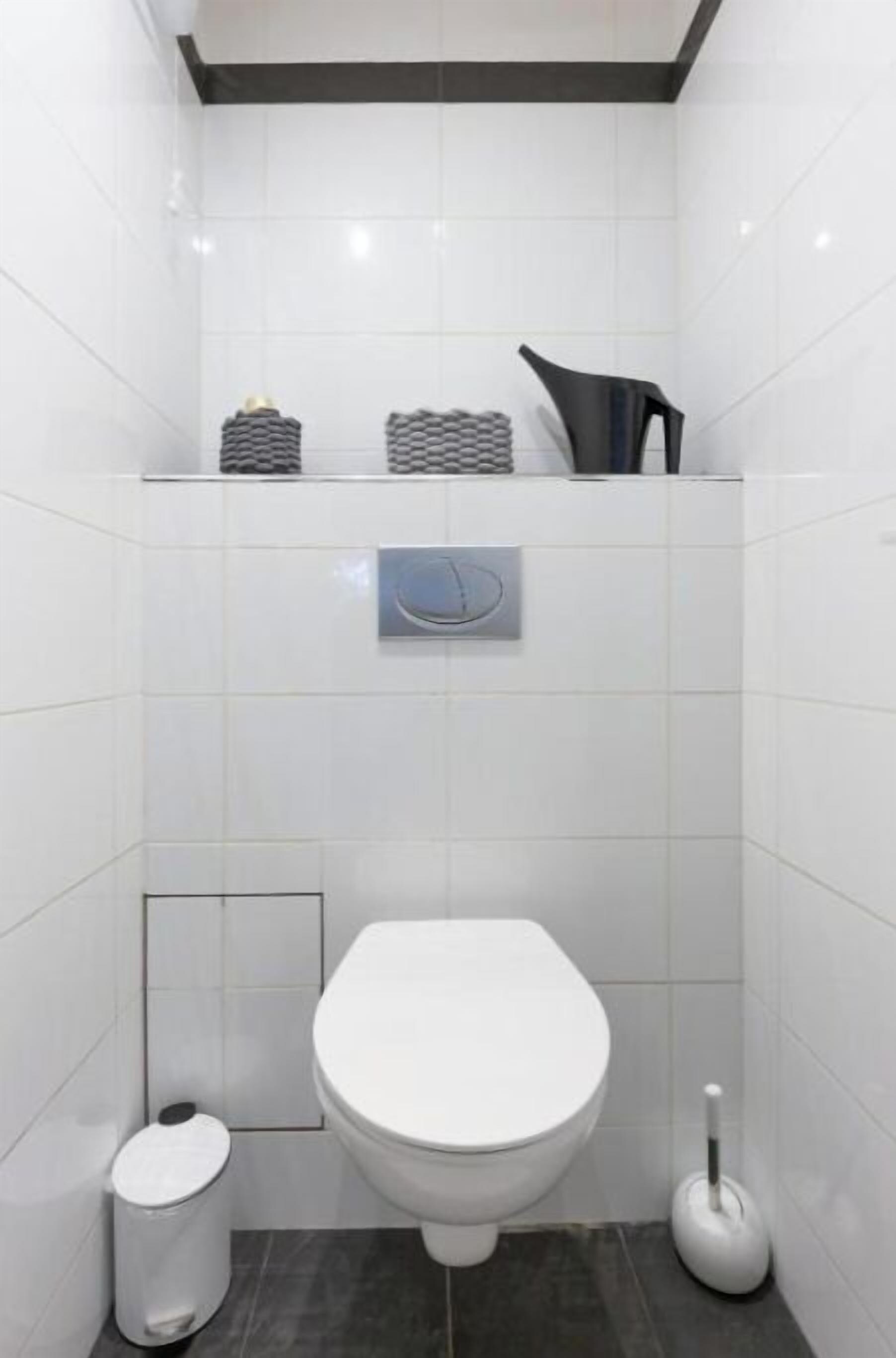 A modern bathroom with a white toilet, a trash bin, and a toilet brush.