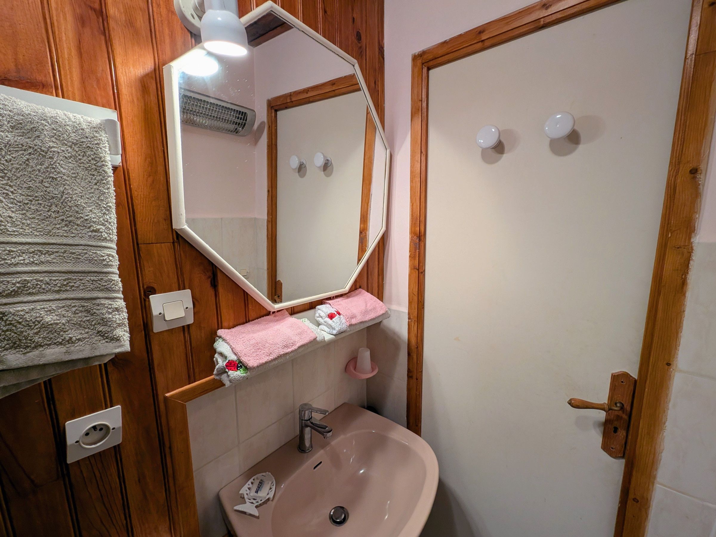 Une salle de bain avec un lambris en bois, un lavabo blanc, un miroir et un porte-serviettes.