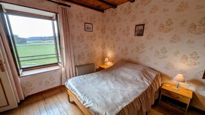 A bedroom with a wooden bed, a window with a view of a green field, and a patterned wallpaper.