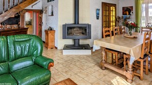 Una sala de estar acogedora con un sofá de cuero verde, una mesa de comedor de madera con sillas, una chimenea y una escalera con vigas de madera.