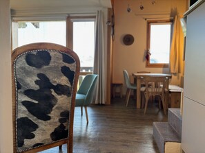 Un comedor con una mesa y sillas de madera, una silla tapizada con cuero de vaca, y vistas al exterior a través de amplios ventanales.