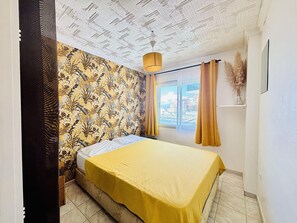 A bedroom with a bed, a window with curtains, a ceiling with a unique pattern, and a hanging light fixture.