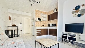 Ein modernes Wohnzimmer mit Sofa, Couchtisch, Fernseher und Küchenzeile mit Mikrowelle und Schränken.