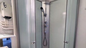 A bathroom with a shower, a hand dryer, and a marble-topped sink.
