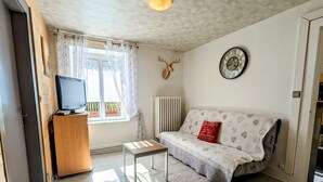 A living room with a sofa, a television on a wooden cabinet, a radiator, and a wall clock.