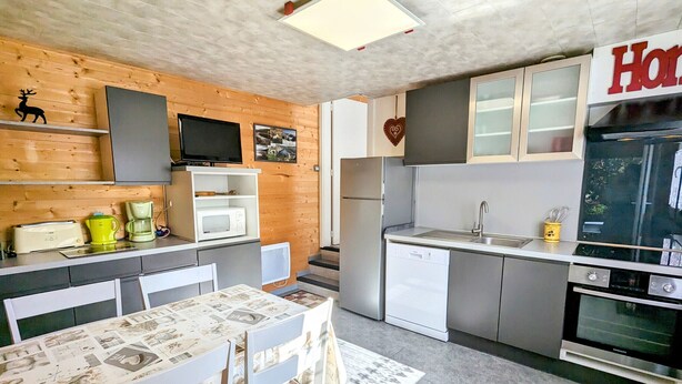 A compact kitchen with a dining area, wooden wall decor, and a visible 'Home' sign.