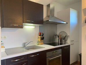 Eine moderne Küche mit dunklen Holzschränken, einer Edelstahl-Dunstabzugshaube, einer Spüle und einem Backofen.