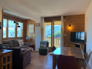 Ein gemütliches Wohnzimmer mit Sofa, Hocker, Esstisch und Fernseher.