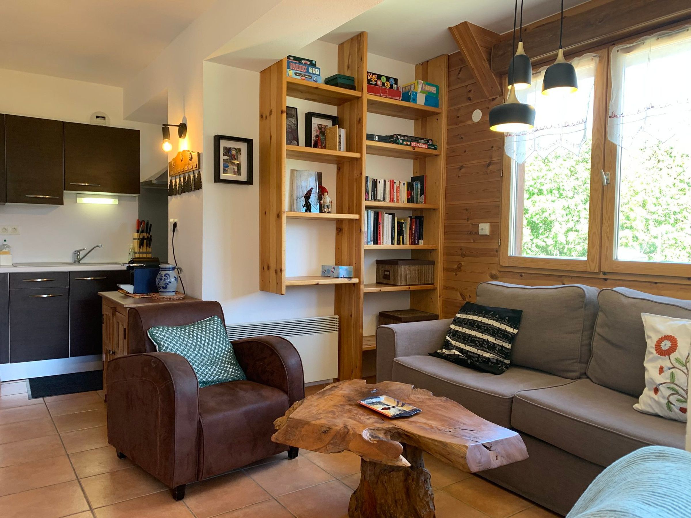 A cozy living room with a sofa, a brown leather chair, a wooden coffee table, and a bookshelf filled with books and games.