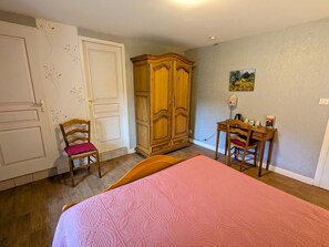 Een slaapkamer met een bed, een kledingkast, een bureau met stoel, en een deur met een stoel ervoor.