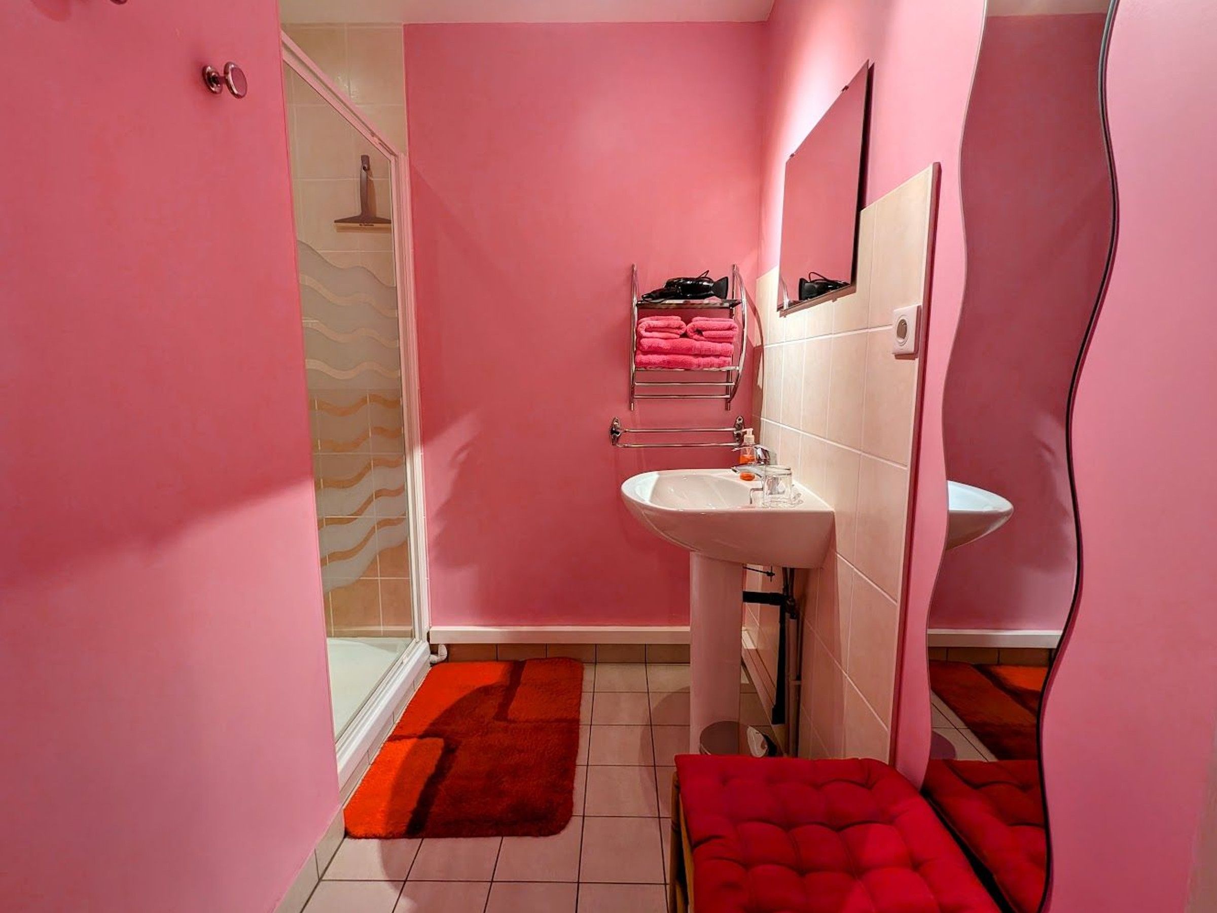 Un baño con paredes rosadas, un lavamanos blanco y una alfombra de baño roja.
