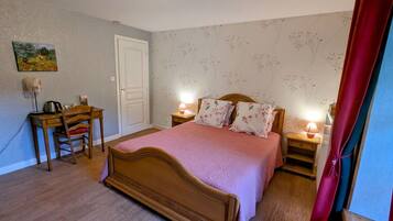 A bedroom with a wooden bed, a desk with a chair, two bedside lamps, and a door.