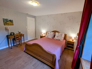 Een slaapkamer met een houten bed, een bureau met stoel, twee bedlampjes en een deur.