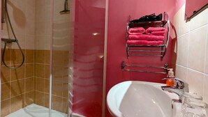 Un baño con cabina de ducha de vidrio, un lavamanos con espejo y un perchero con toallas rosas.