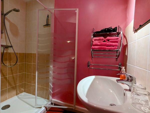 Une salle de bain avec une douche à parois de verre, un lavabo avec un miroir et un porte-serviettes avec des serviettes roses.
