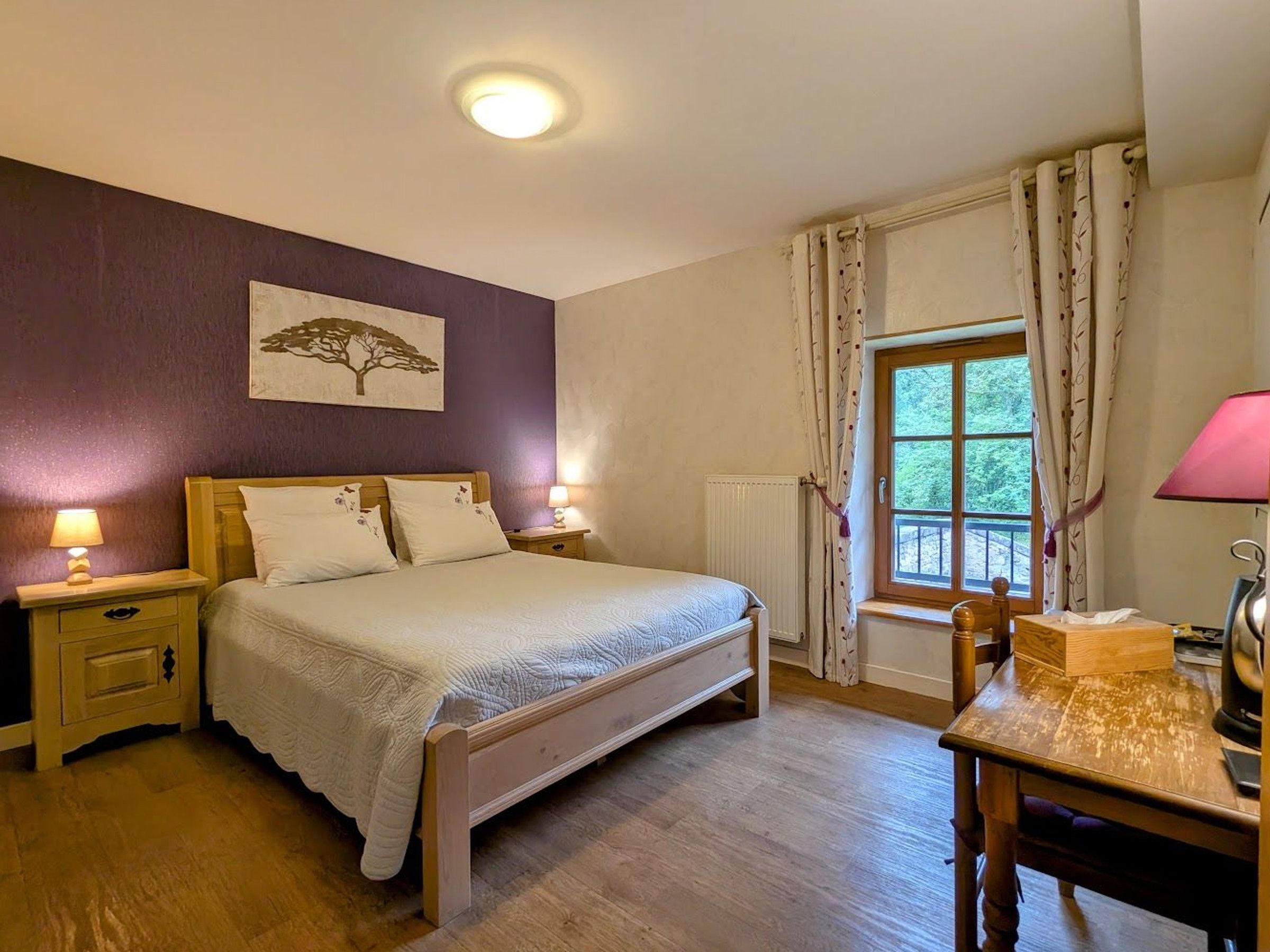 Une chambre à coucher avec un lit en bois, deux tables de chevet avec des lampes, une fenêtre avec des rideaux et un tableau accroché au mur.