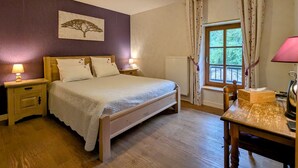Un dormitorio con una cama de madera, dos mesitas de noche con lámparas, un ventanal con cortinas y un cuadro en la pared.