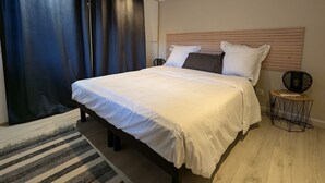 A modern bedroom with a large bed, dark curtains, a wooden headboard, and a small side table. - Cozy studio with terrace near Epinal, parking included (Dinozé)