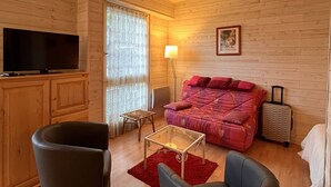 A cozy log cabin room with a large TV, a red rug, a wooden cabinet, and a red sofa.