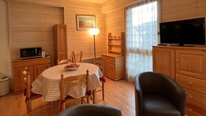 A cozy room with a wooden interior, a dining table with chairs, a television, and a lamp.