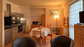 A compact kitchen with modern appliances, a dining area with a table and chairs, and a television on a wooden cabinet.