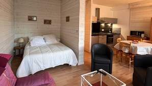 A compact room with a bed, a small table, a chair, and a kitchenette.