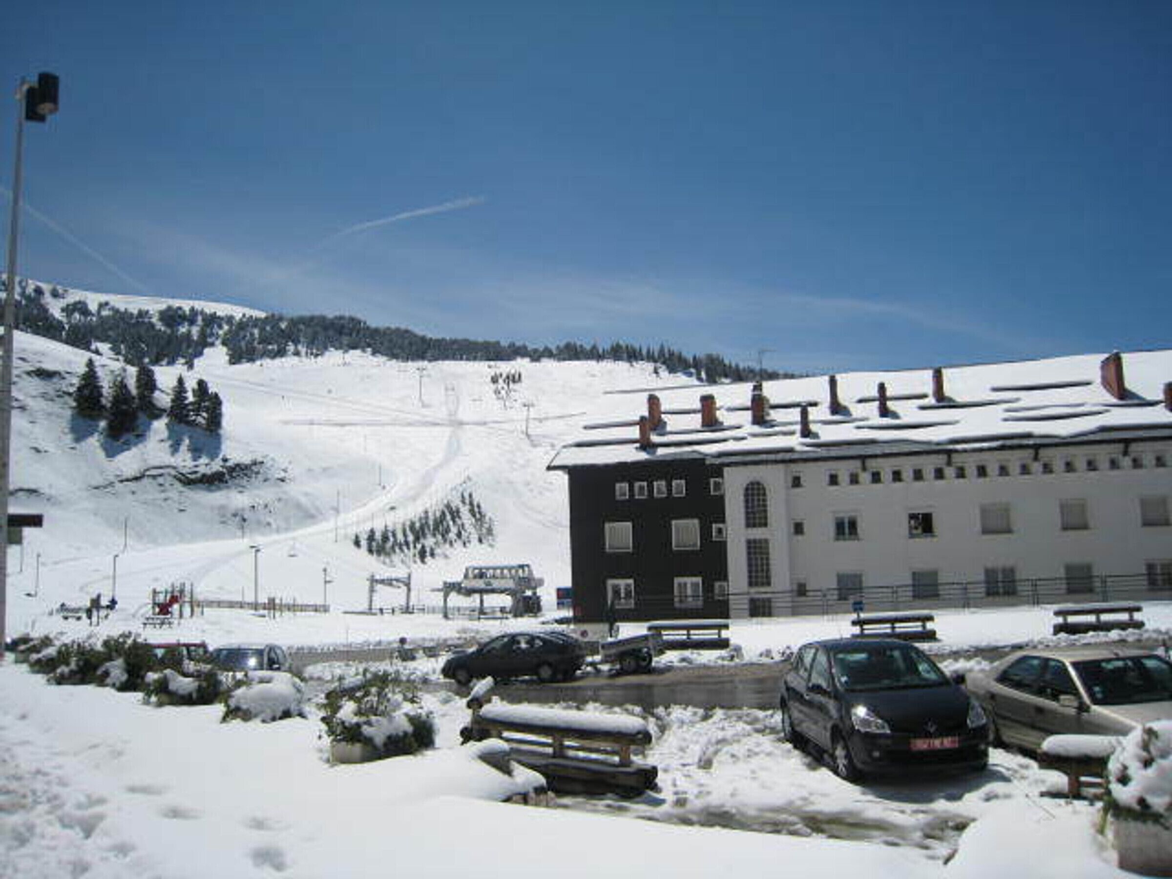 Et hotel med en skilift i baggrunden, en parkeringsplads med biler og et sneklædt landskab.