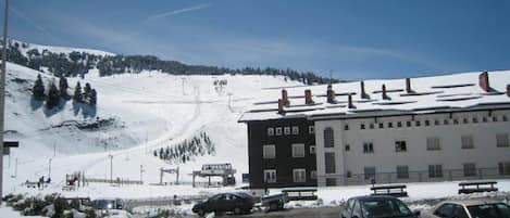A hotel with a ski lift in the background, a parking area with cars, and a snowy landscape.