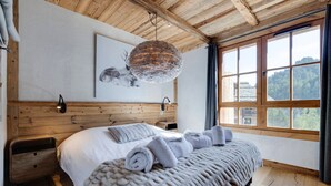 A bedroom with a wooden ceiling, a large bed with rolled towels, a wall-mounted light, and a window with a view of trees. - Arc 1950: 10 guests, 4 bdr, ski-in/ski-out (Les Arcs 1950)
