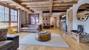 A spacious living room with wooden beams, a sofa, a coffee table, and a dining area. - Arc 1950: 10 guests, 4 bdr, ski-in/ski-out (Les Arcs 1950)