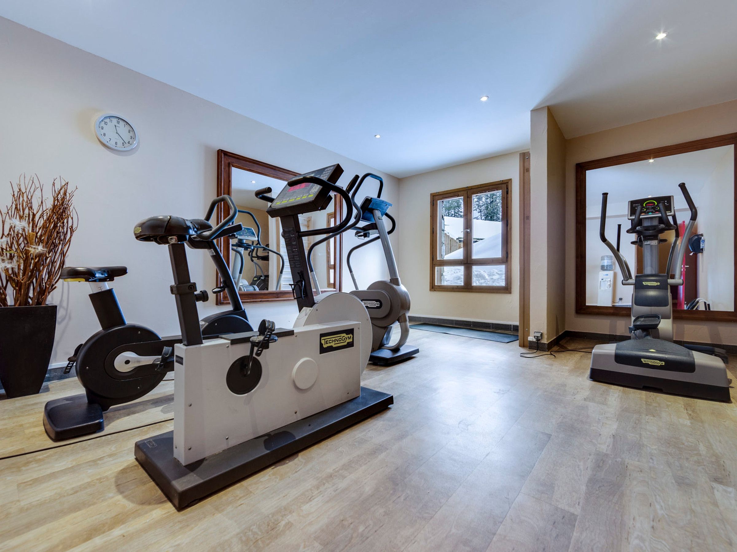 A gym with various exercise equipment, large windows, and a clock on the wall.