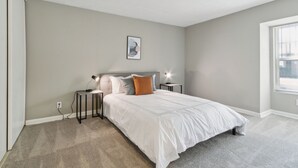 A bedroom with a bed, nightstands, a wall-mounted lamp, and a window.