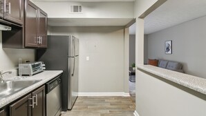A kitchen with dark cabinets, a stainless steel refrigerator, a toaster, and a sink.