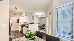 A modern kitchen with white cabinets, a marble dining table, and a potted plant.
