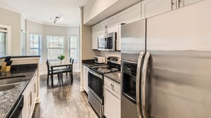 A modern kitchen with stainless steel appliances, a dining area with a table and chairs, and large windows allowing natural light.