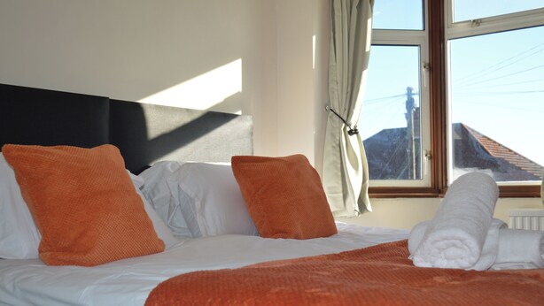 Camera d'albergo con un letto, cuscini arancioni, biancheria da letto bianca, una finestra vista edifici e un termosifone.