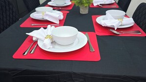 Una tavola da pranzo imbandita con tovaglia bianca, sottopiatti rossi e sedie nere.
