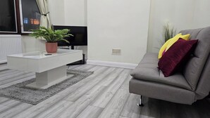 Un soggiorno moderno con un divano grigio, un tavolino da caffè bianco con una pianta e una televisione a schermo piatto.