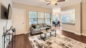 A living room with a sofa, coffee table, and a ceiling fan. There is a door and a window with blinds.