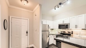 A modern kitchen with white cabinets, stainless steel appliances, and a marble countertop.