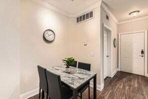 A dining area with a marble table, black chairs, a potted plant, a wall clock, and a white door.