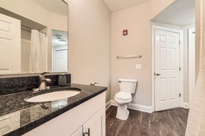A bathroom with a granite countertop sink, a white toilet, and a door leading to another room.
